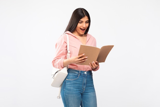 Estudiante emocionada mirando el libro de texto en un fondo blanco de alegría