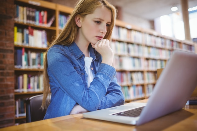 Estudiante enfocado que usa la computadora portátil en biblioteca