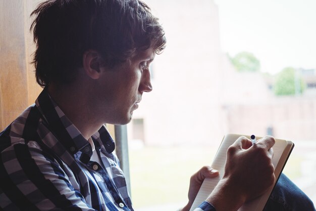 Estudiante escribiendo notas cerca de la ventana