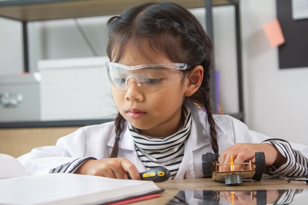Estudiante de la escuela haciendo autos robóticos Niña en la escuela de robótica hace que el robot sea manejado por el constructor el niño aprende a construir el robot