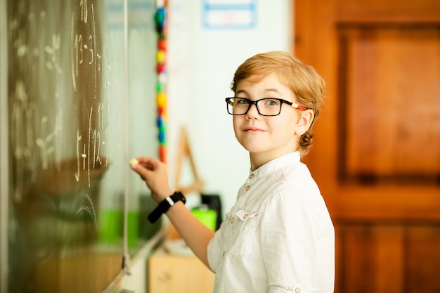 Estudiante de escuela primaria con gafas negras escribiendo matemáticas respuesta en pizarra