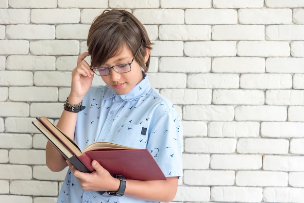 Estudiante de escuela secundaria con anteojos en el libro de lectura para los exámenes finales