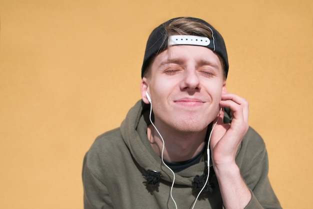 Un estudiante está escuchando música con auriculares en una pared naranja, y los trucos están arrancados.