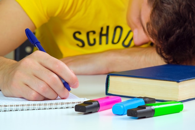 el estudiante está sentado en una mesa con un libro de texto y un cuaderno, sintiéndose aburrido. El tema tiene poco interés, es demasiado perezoso para realizar tareas.