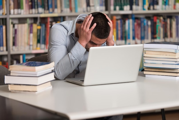 Estudiante estresado de la escuela secundaria sentado en el escritorio de la biblioteca Profundidad de campo