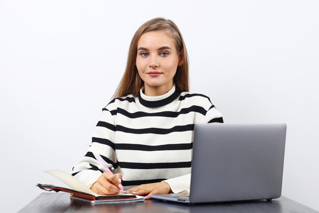 Una estudiante europea con una sudadera a rayas se sienta en un escritorio y obtiene conocimientos a través de una computadora portátil