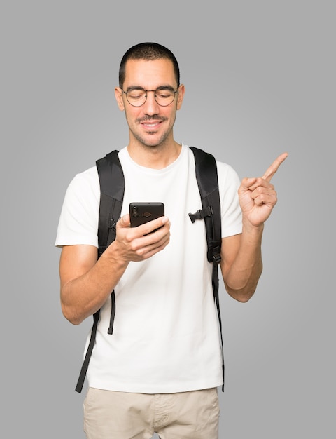 Estudiante feliz apuntando hacia arriba y usando un teléfono móvil