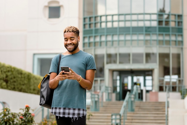 Estudiante feliz comprobando el teléfono móvil en el campus