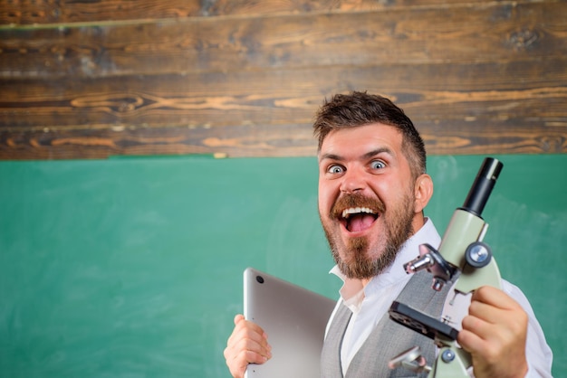 Estudiante feliz con computadora portátil y microscopio hombre barbudo con cuaderno y microscopio biología o