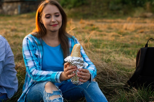 La estudiante feliz descansa al aire libre y come un perrito caliente