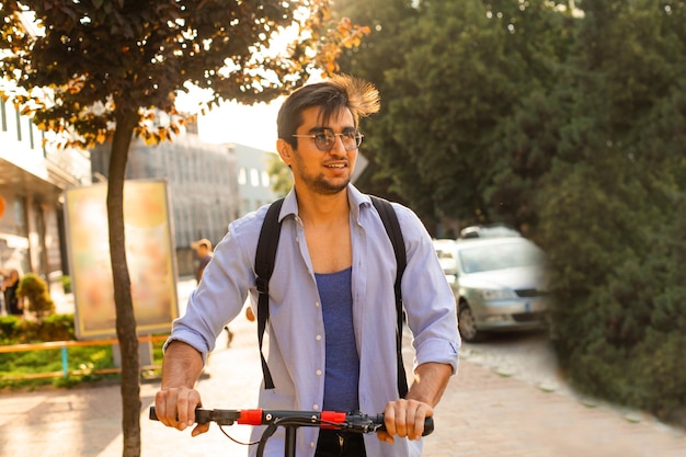 Foto el estudiante feliz monta un scooter eléctrico en la ciudad.