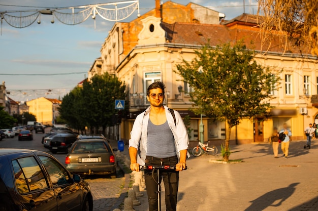 El estudiante feliz monta un scooter eléctrico en la ciudad.