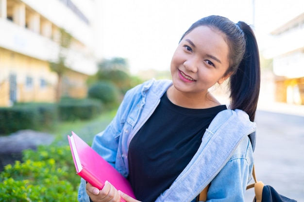 Una estudiante feliz sostiene un libro y una mochila en la escuela, una chica asiática.