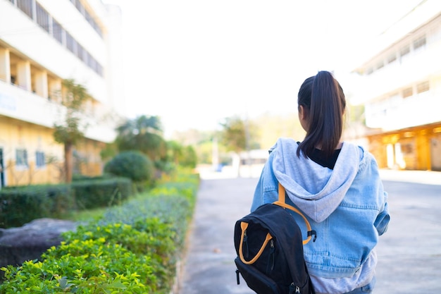 Una estudiante feliz sostiene un libro y una mochila en la escuela, una chica asiática.