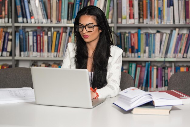 Estudiante feliz trabajando con un portátil en la biblioteca