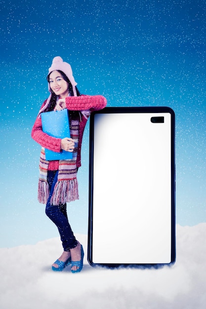 Estudiante femenina apoyándose en el celular bajo la nieve