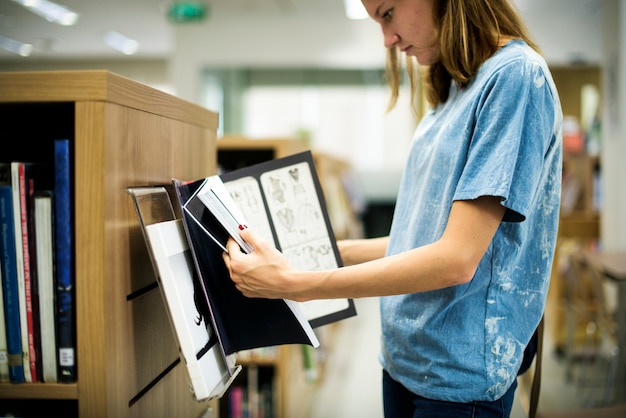 Estudiante femenina hojeando un libro en la biblioteca