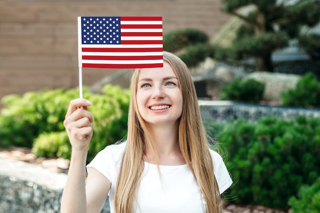 Estudiante femenina mira la pequeña bandera estadounidense y se encuentra en el contexto de la universidad y sonriendo