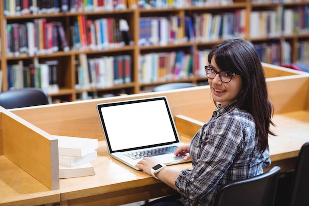 Estudiante femenino sonriente que usa la computadora portátil en biblioteca