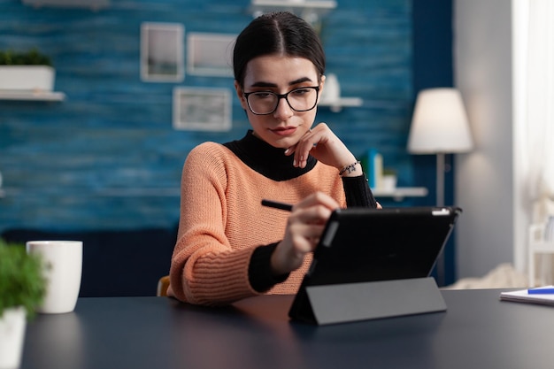 Estudiante con gafas sosteniendo lápiz táctil tocando la pantalla de la tableta. Programador en la oficina en casa interactuando con tablet-pc. Freelancer en estudio mirando casualmente la pantalla mientras sostiene el lápiz táctil.