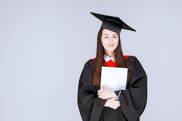 Estudiante graduado con papel y bolígrafo de pie antes de que comience la ceremonia. Foto de alta calidad