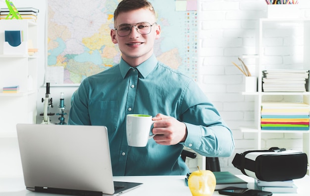 Estudiante guapo feliz en espectáculos con una calificación excelente para el examen Retrato de estudiante masculino feliz trabaja en la computadora portátil sostiene una taza de té o café