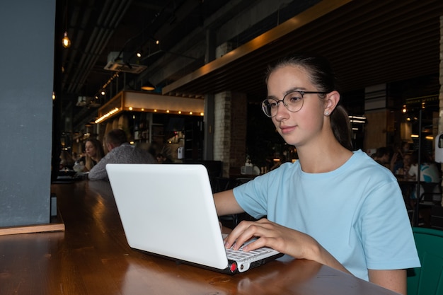 Estudiante hermosa chica usando una computadora portátil, escribiendo un mensaje, buscando en Internet sentado en una mesa en un café tipo loft. Concepto de autónomo.