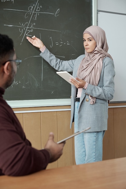 Estudiante en hijab apuntando a la pizarra mientras explica el nuevo tema