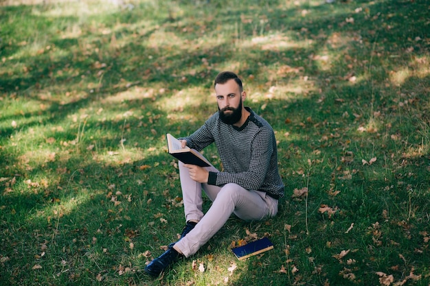 Estudiante hipster barbudo leyendo un libro al aire libre