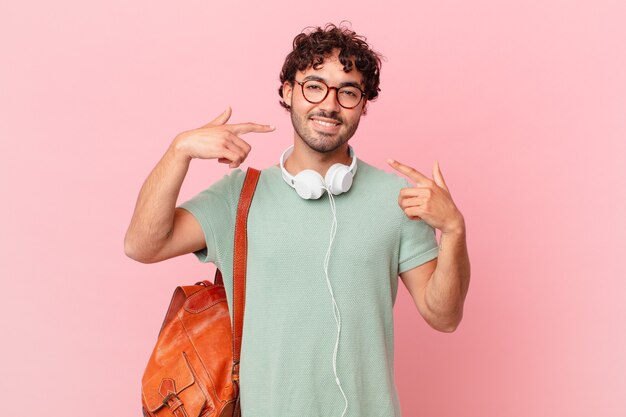 Estudiante hispano sonriendo con confianza apuntando a su propia sonrisa amplia, actitud positiva, relajada y satisfecha