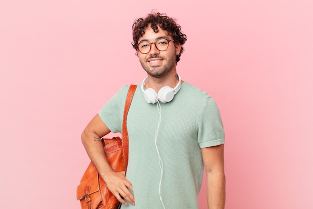 Estudiante hispano sonriendo felizmente con una mano en la cadera y actitud confiada, positiva, orgullosa y amistosa