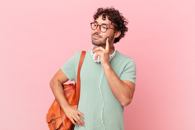 Estudiante hispano sonriendo felizmente y soñando despierto o dudando, mirando hacia un lado