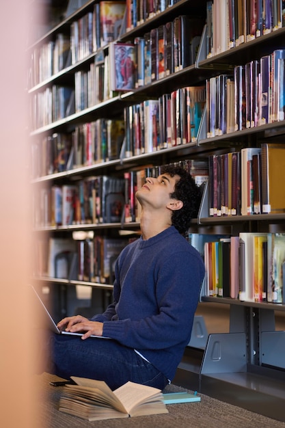 Estudiante hombre multitarea usando una computadora portátil para estudiar sentado en el suelo en el campus de la biblioteca universitaria