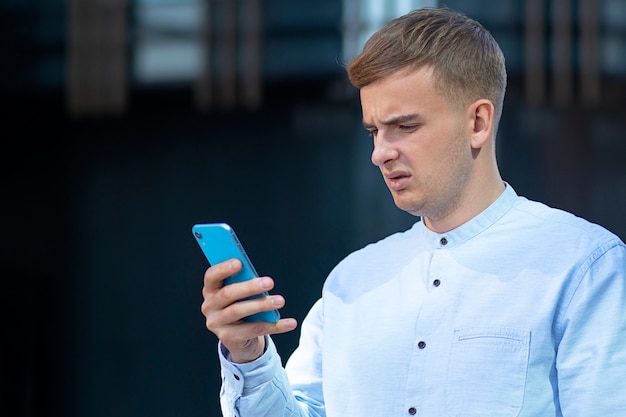 Estudiante imprime mensaje, hombre disgustado en su teléfono inteligente móvil. Hombre enojado joven empresario