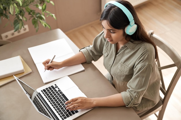 Una estudiante india usa auriculares viendo una clase de seminario web en línea y aprende en casa