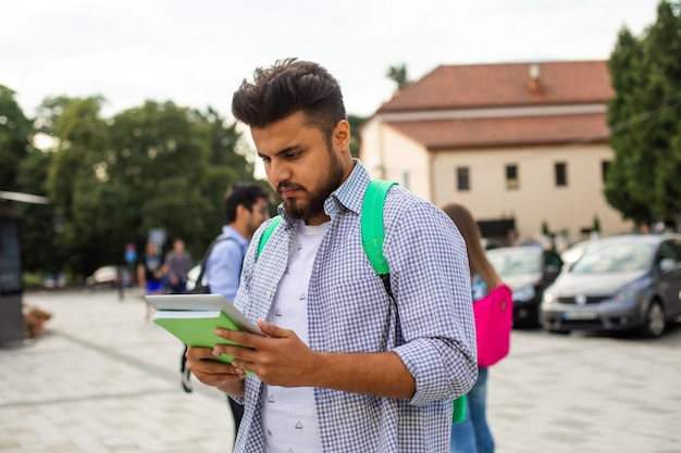 El estudiante indio se para al aire libre y sostiene una pila de libros.