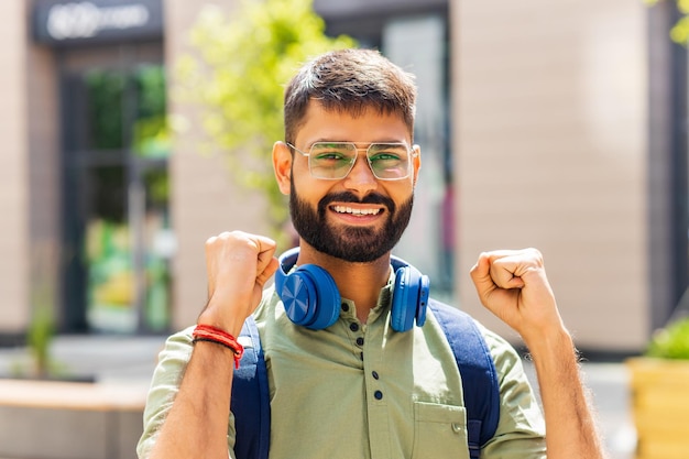 Estudiante indio con auriculares azules y mochila mirando bien el día soleado