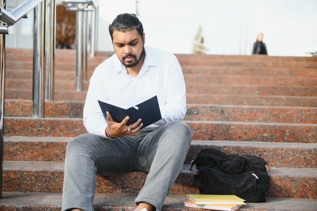 Estudiante indio feliz sentado en las escaleras del campus universitario