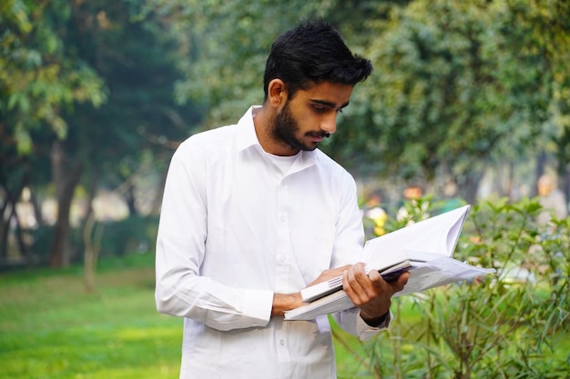 Estudiante indio leyendo un libro cerca del campus universitario