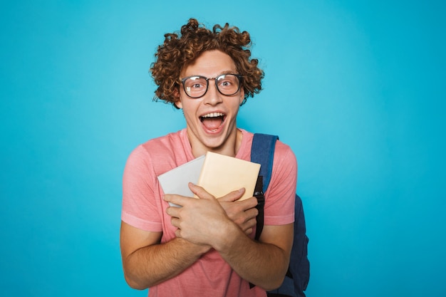 Estudiante inteligente con cabello rizado con gafas y mochila sonriendo y sosteniendo libros