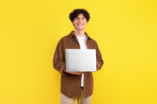 Estudiante inteligente con computadora portátil usando computadora sobre fondo amarillo