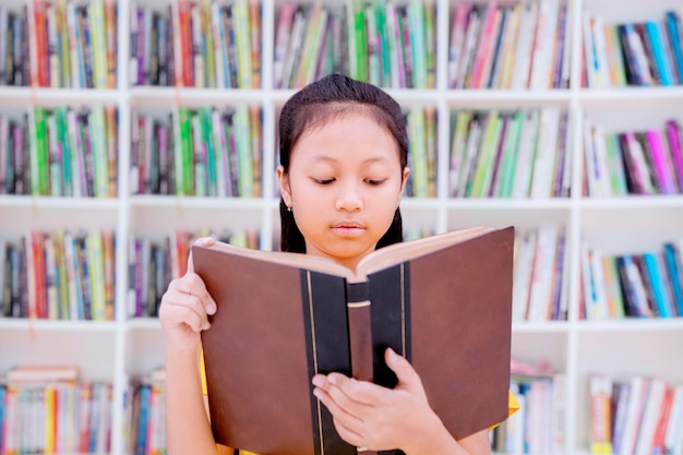 Una estudiante inteligente leyendo un libro en la biblioteca.