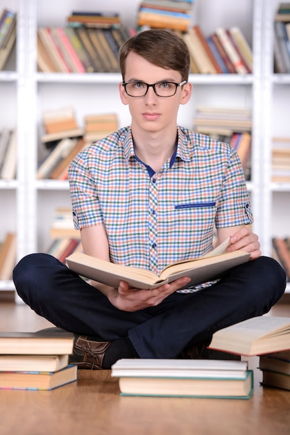 Estudiante inteligente con libro abierto leyéndolo en la biblioteca de la universidad.