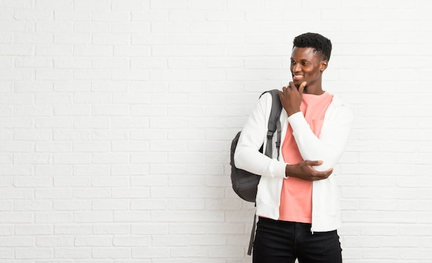 Estudiante joven del afroamericano que se coloca y que mira al lado con la mano en la barbilla