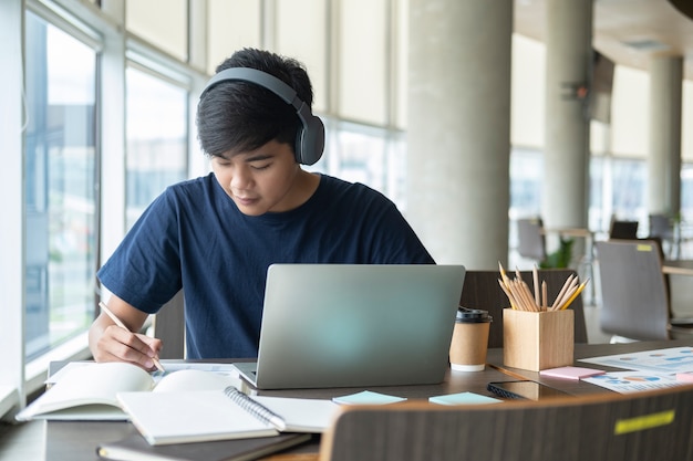 Estudiante joven del collage que usa la computadora y el dispositivo móvil que estudia en línea.