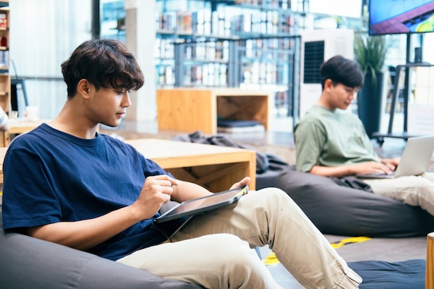 Estudiante joven del collage que usa la computadora y el dispositivo móvil que estudian en línea. Educación y aprendizaje en línea.