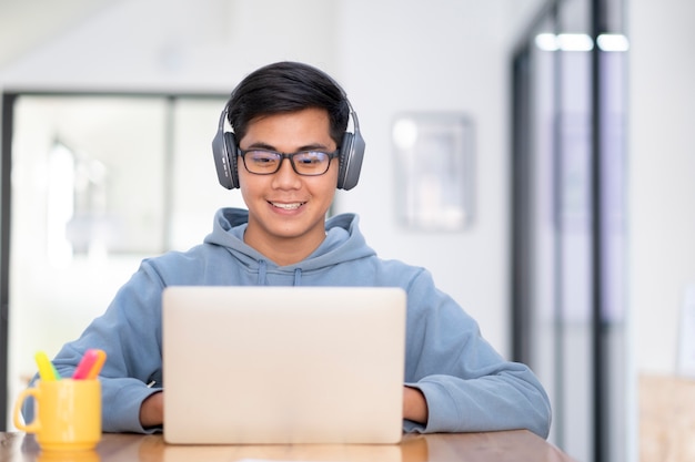 Estudiante joven del collage que usa la computadora y el dispositivo móvil que estudian en línea.