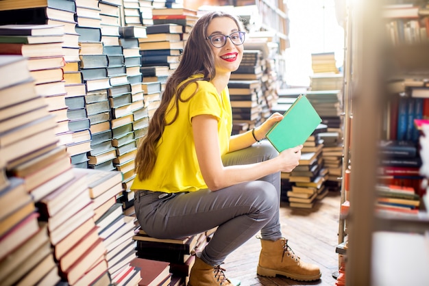 Estudiante joven escuchando la música sentado en el montón de libros en la antigua biblioteca