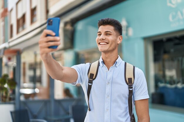 Estudiante joven hispano haciendo selfie por el teléfono inteligente en la calle