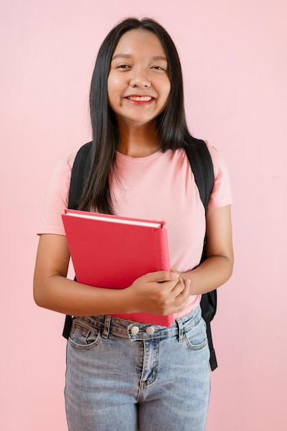 Estudiante joven con libro y mochila sobre fondo rosa